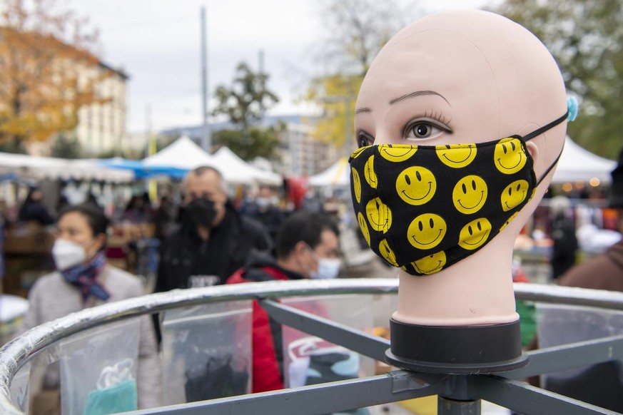 Une tete de mannequin presente une masque de protection avec des smileys sourires devant des personnes portant des masques de protection contre la propagation du coronavirus COVID-19, sur les stands d ...