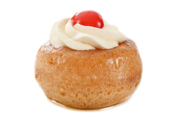rum baba with cream and cherry in front of white background