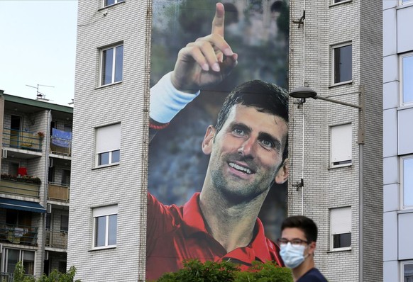 epa08506276 A man wearing a protective face mask walks past a huge billboard depicting Serbian tennis player Novak Djokovic in Belgrade, Serbia, 24 June 2020. Djokovic released a statement on 23 June  ...