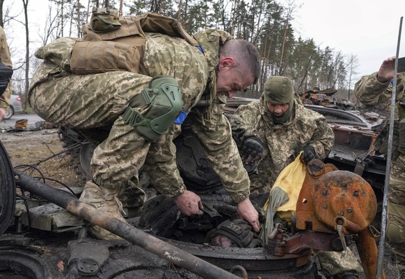 Ukrainian soldiers work to remove the body of a Russian soldier from a destroyed Russian tank, in the village of Dmytrivka close to Kyiv, Ukraine, Saturday, April 2, 2022. At least ten Russian tanks w ...