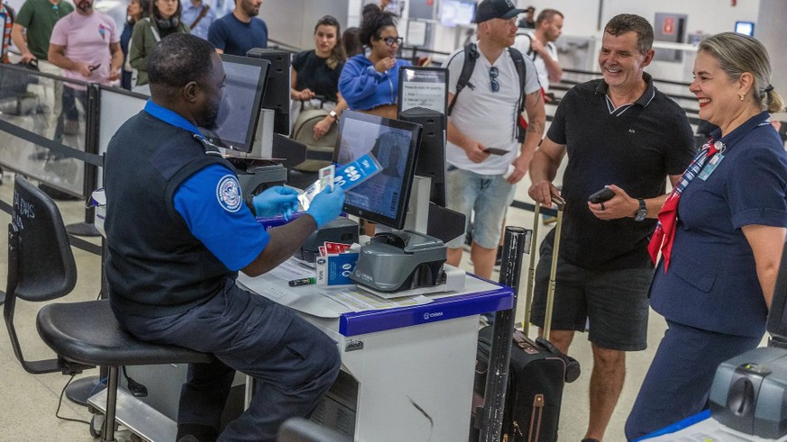 Un employé vérifie les passeports des passagers à l'aéroport international de Miami. Il doit maintenant se tenir debout.