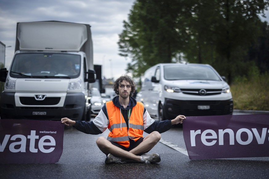 epaselect epa10699493 An environmental activist of &#039;Renovate Switzerland&#039; civil resistance campaign holds banners while sitting down on the road during a roadblock action on the motorway A1  ...
