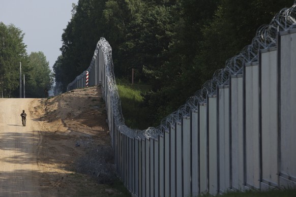 FILE - A Polish border guard patrols the area of a built metal wall on the border between Poland and Belarus, near Kuznice, Poland, on June 30, 2022. Poland is deploying thousands of troops to its bor ...