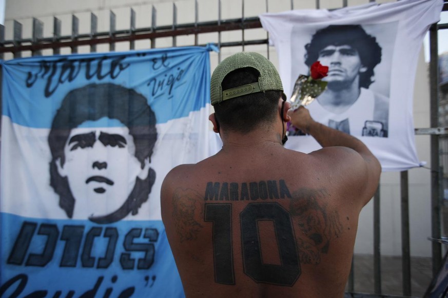 A man places a flower on a jersey with the face of late soccer star Diego Maradona during a march to demand answers regarding his death, in Buenos Aires, Argentina, Wednesday, March 10, 2021. An inves ...