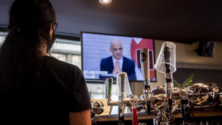 A waitress wearing a protective mask reacts while watching on a TV screen Swiss Interior and Health Minister Alain Berset as he speaks during a press conference in Bern announcing new measures against ...