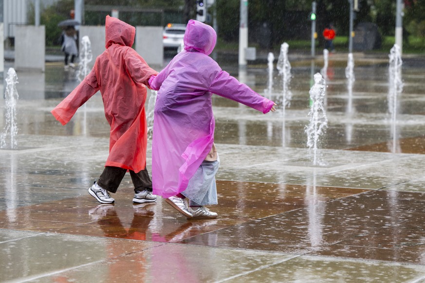 Des touristes se promenent avec leurs pelerine sous la pluie et face aux jets de la fontaine de la place des Nations, ce jeudi 26 septembre 2024 a Geneve. Meteo Suisse annonce une alerte de niveau tro ...