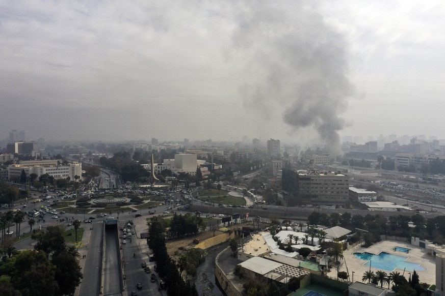 Smoke billows in the background as residents and opposition fighters celebrate in a central square after opposition forces took control of the city in Damascus, Syria, Sunday, Dec. 8, 2024. (AP Photo/ ...