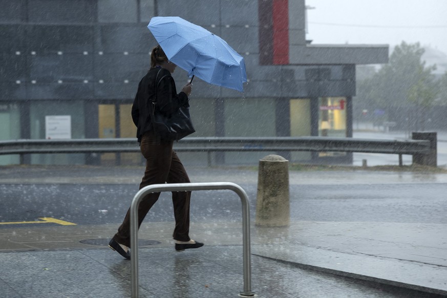 Une femme marche rapidement sous la pluie abritee de son parapluie lors du passage orageux sur la ville, ce mercredi 17 aout 2022 a Geneve. (KEYSTONE/Salvatore Di Nolfi)