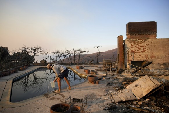 Garrett Yost gathers water from a pool while surveying his neighbors&#039; fire-ravaged properties in the aftermath of the Palisades Fire in the Pacific Palisades neighborhood of Los Angeles, Friday,  ...