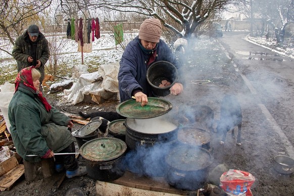 epa10328480 Local woman Yelena (C) cooks porridge for dogs on the outdoor fire on her home in Cherkaski Tyshky, Kharkiv region, Ukraine, 25 November 2022. Yelena and her assistants took patronage over ...