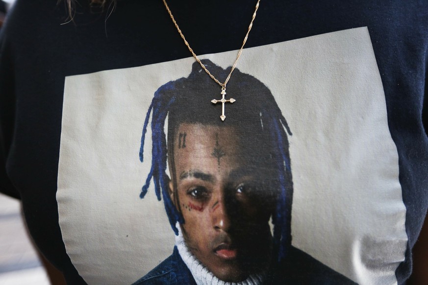 FILE- In this June 27, 2018, file photo a fan wears a cross around her neck dangling on a t-shirt in remembrance before she enters a memorial for the rapper, XXXTentacion in Sunrise, Fla. A Florida ju ...