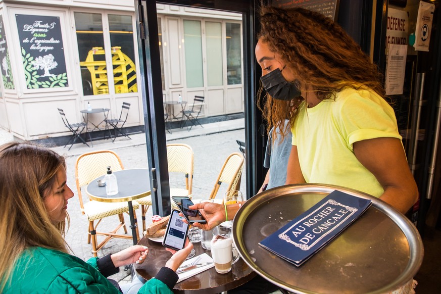 epa09407132 Customers show their QR codes to a waiter at a bar in Paris, France, 09 August 2021. Starting from 09 August, the Covid-19 pass will be required in France to access cafes, restaurants, lon ...