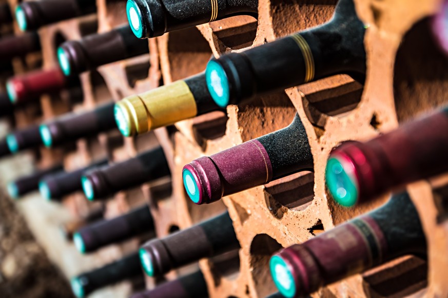 Selective focus of wine rack on wall in brick material full, to store red wine bottle in a row in cellar, cool and in good conditions.Some of those are old wine bottle with dust.