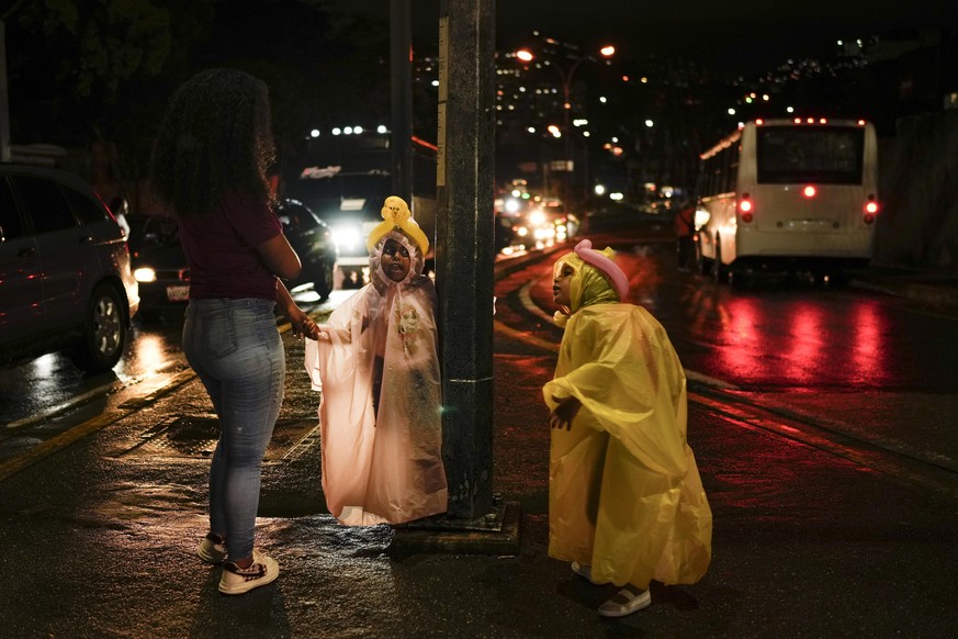 Girls wearing rain covers wait for a public bus with their mother in the Catia neighborhood of Caracas, Venezuela, Saturday, Oct. 8, 2022. (AP Photo/Matias Delacroix)