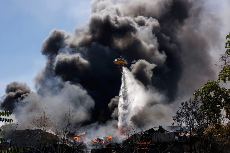 Un hélicoptère largue de l'eau sur un incendie qui s'est déjà propagé aux habitations.
