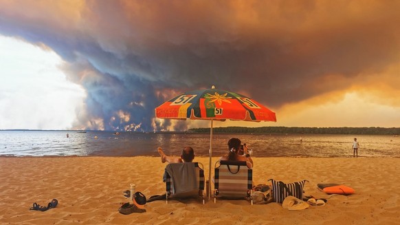 Beach goers sit on the beach of Moutchic in Lacanau, southwestern France on July 24, 2026, as clouds of smoke rise into the sky from a wildfire. The fire raging in the northern part of the Arcachon Ba ...