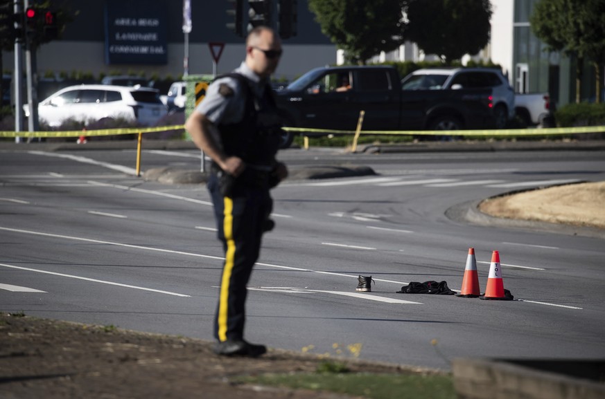 An RCMP officer stands near a shoe with blood on it and other belongings on the road at the scene of a shooting in Langley, British Columbia, Monday, July 25, 2022. Canadian police reported multiple s ...