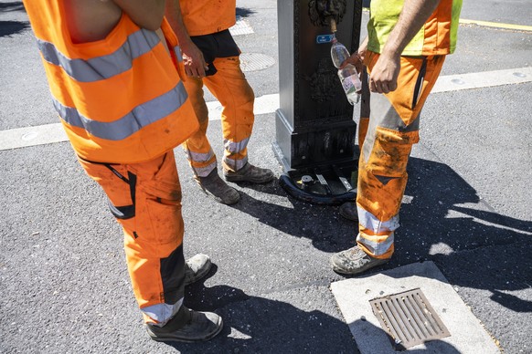 Un ouvrier rempli une bouteille d?eau a un fontaine publique devant ces collegues avant de retourner travailler sur la route a la pose d?un nouveau revetement, un enrobe bitumineux de goudron phonoabs ...