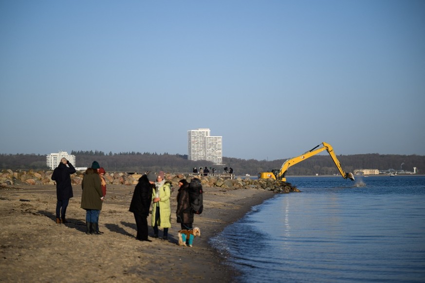 Onlookers stand on the beach in Niendorf, northern Germany, on March 27, 2026, with heavy machinery still visible in the background after a humpback whale that had run aground off the Baltic Sea coast ...