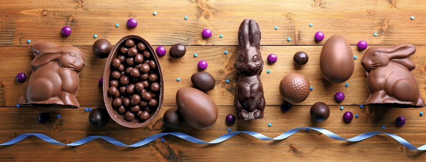 Easter background greeting card with holiday traditional confectionery, Easter egg hunt fun concept. Chocolate bunny, chocolate and candy Easter eggs on wooden background
