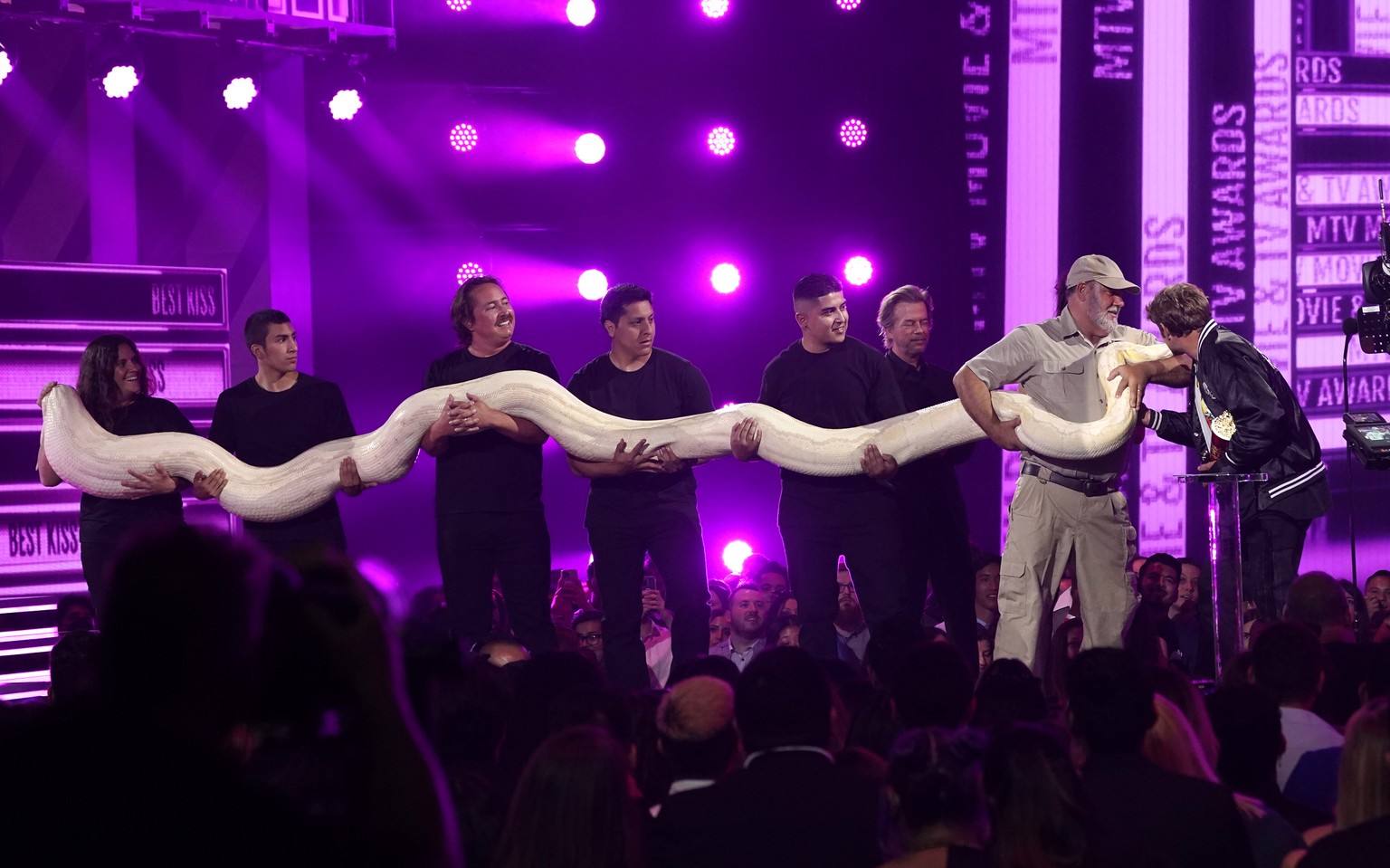 Handlers hold an anaconda as Sean &quot;Poopies&quot; McInerney, right, accepts the best kiss award at the MTV Movie and TV Awards on Sunday, June 5, 2022, at the Barker Hangar in Santa Monica, Calif. ...