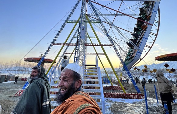 Afghan men walk past a swing near Kabul, Afghanistan, Friday, Feb. 11, 2022. Six months since Kabul was ceded to the Taliban with the sudden and secret departure of U.S.-backed president residents say ...