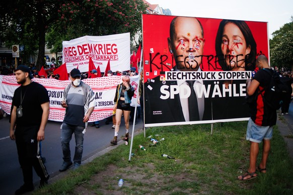 epa11313376 Protesters with a banner reading &#039;War to the war&#039; pass by a Social Democrats campaign poster showing German Chancellor Olaf Scholz and Vice-President of the European Parliament a ...