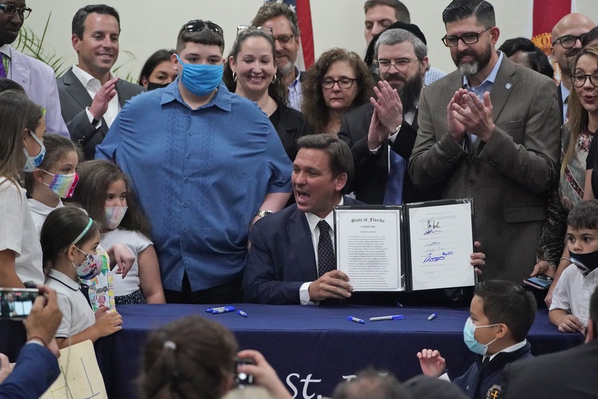 Florida Gov. Ron DeSantis, seated, celebrates after having signed a bill Tuesday, May 11, 2021, that increases eligibility to attend private schools at public expense, during a ceremony at St. John th ...