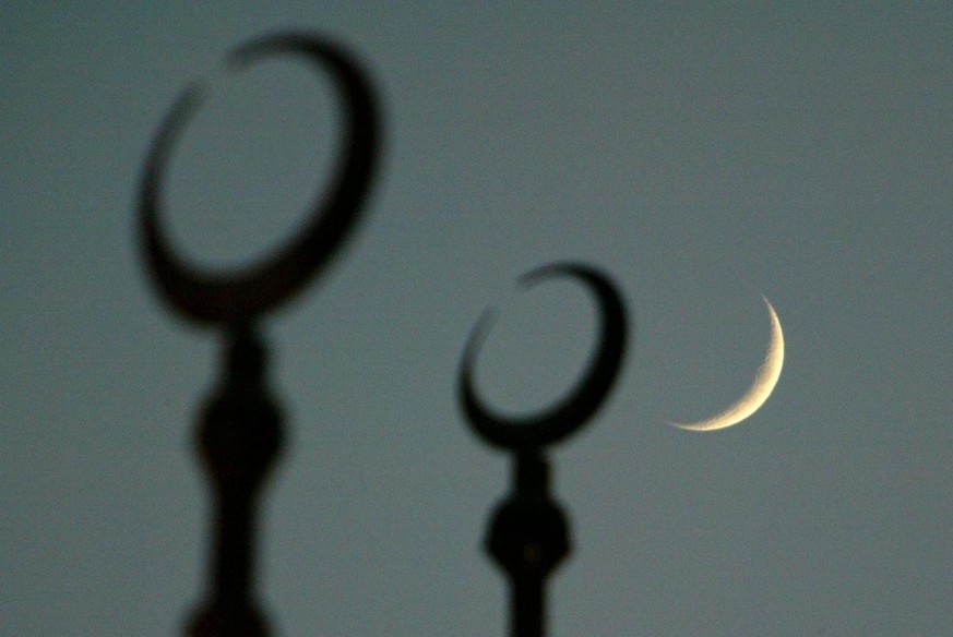 The moon seen behind the silloutte of the crescents on top of the dome of the Cultural Square Mosque, on the second evening of Ramadan, the Muslim holy month of fasting, in Sharjah, United Arab Emirat ...