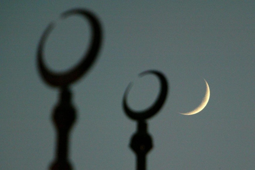 The moon seen behind the silloutte of the crescents on top of the dome of the Cultural Square Mosque, on the second evening of Ramadan, the Muslim holy month of fasting, in Sharjah, United Arab Emirat ...