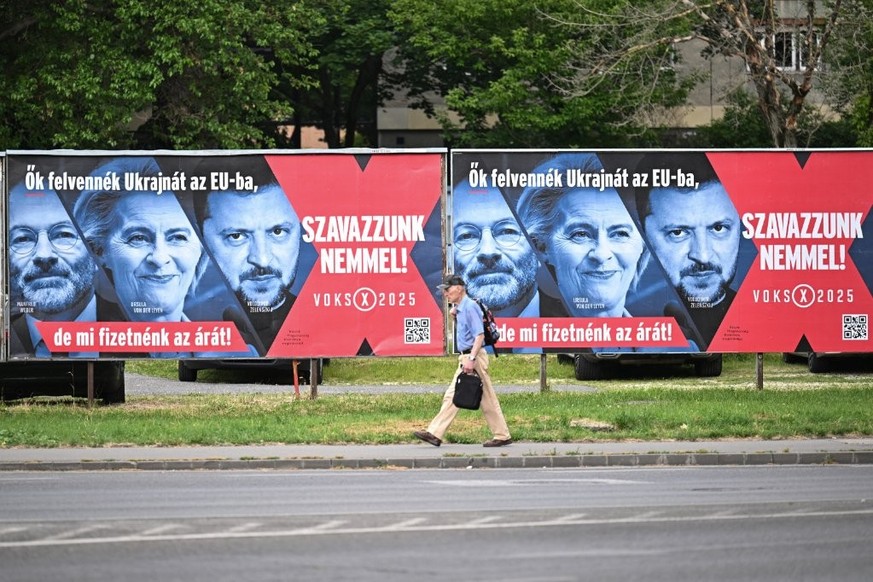 Cette photo montre un piéton passant devant des panneaux d'affichage faisant partie d'une campagne du gouvernement hongrois avec le slogan «Ils admettraient l'Ukraine dans l'UE, ma ...