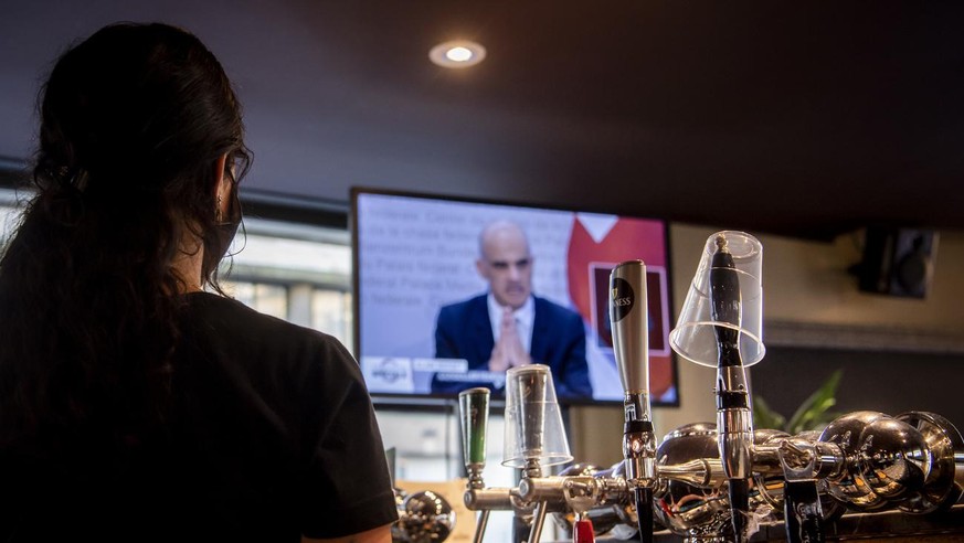 A waitress wearing a protective mask reacts while watching on a TV screen Swiss Interior and Health Minister Alain Berset as he speaks during a press conference in Bern announcing new measures against ...