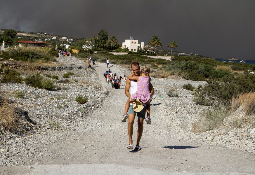 A man carries a child as they leave an area where a forest fire burns, on the island of Rhodes, Greece, Saturday, July 22, 2023. A large wildfire burning on the Greek island of Rhodes for a fifth day  ...