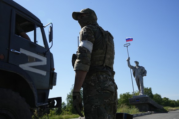 A military truck with the letter Z, which has become a symbol of the Russian military, drives past a Russian soldier standing in the road at the entrance of Mariupol with a Soviet style symbolic monum ...