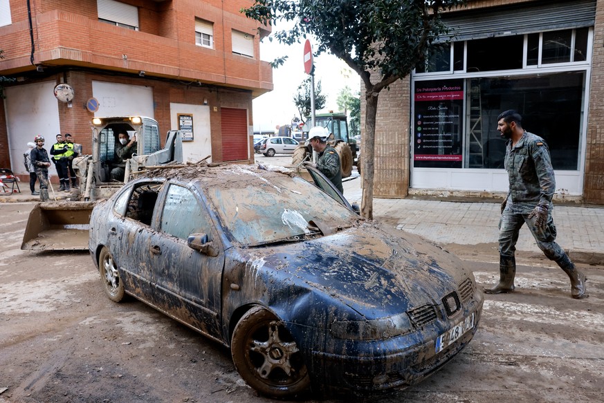 epa11729523 Military Emergency Unit (UME) personnel stand beside a mud-covered car during clean up operations in the flood-affected municipality of Catarroja, province of Valencia, eastern Spain, 19 N ...