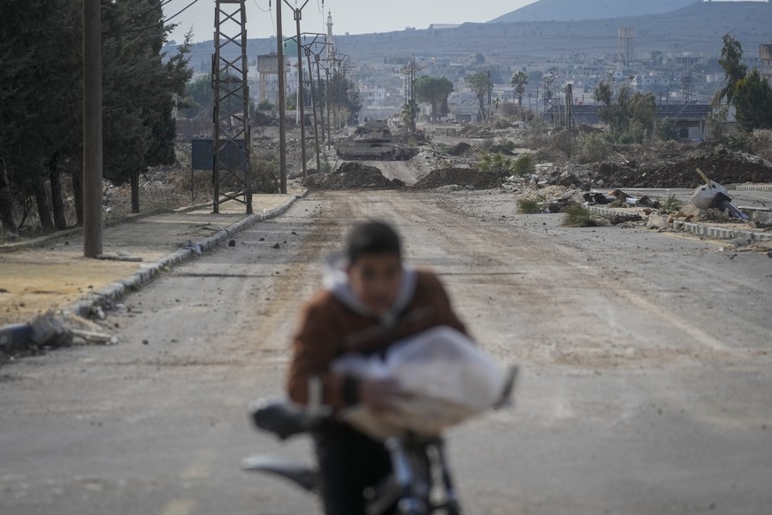 A boy rides his bicycle on a road blocked by Israeli army armoured vehicles in the outskirts of the town of Quneitra, Syria, Sunday Jan. 5, 2025.(AP Photo/Mosa'ab Elshamy)