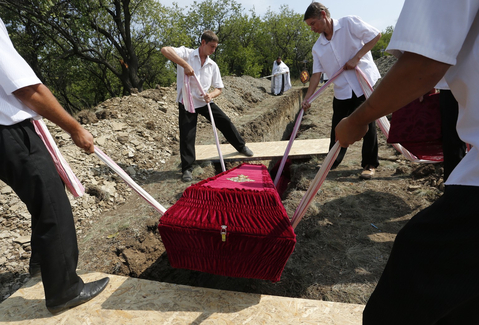 epa09438722 Workers lower a coffin to a grave during a funeral ceremony of 30 civilians, who were exhumed from a mass grave a week ago near Irmino village not far from Pervomaysk in self-proclaimed Lu ...