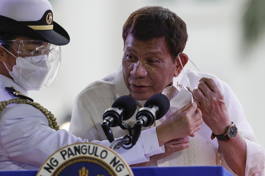 Philippine President Rodrigo Duterte is assisted as he removes his face mask before delivering his speech during the 123rd anniversary of the proclamation of the Philippine independence rites on Satur ...