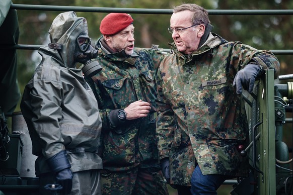 epa10527181 German Defense Minister Boris Pistorius (R) talks to Commander NBC Defense Command of the German Armed Forces, Colonel Stephan Saalow (C), next to a soldier with a gas mask in an NBC suit  ...