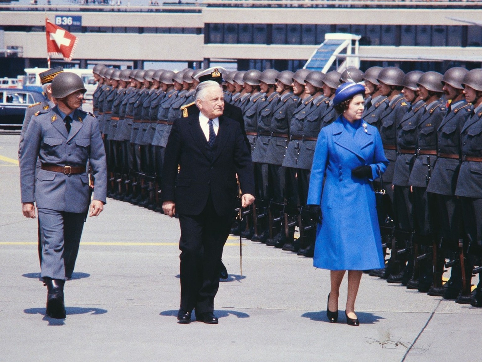 Visite officielle de la reine Élizabeth II en Suisse en 1980. La souveraine passe en revue la garde d’honneur à l’aéroport de Zurich-Kloten en compagnie du président de la Confédération Georges-André  ...