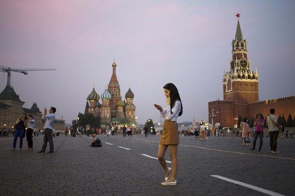 A young woman holds her smartphone at Red Square with the Kremlin&#039;s Spasskaya Tower, right, and St. Basil Cathedral, center, in the background in Moscow, Russia, Monday, July 25, 2016. (AP Photo/ ...