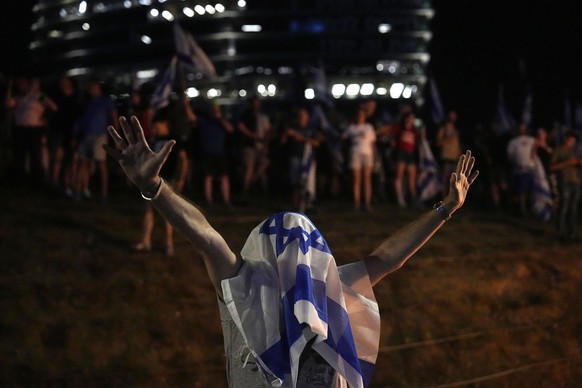 A person wears the Israeli national flag while protesting against plans by Prime Minister Benjamin Netanyahu&#039;s government to overhaul the judicial system, in Tel Aviv, Thursday, July 20, 2023. (A ...