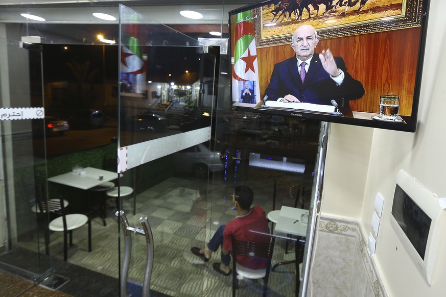 A man sits outside a restaurant while Algerian President Abdelmadjid Tebboune speaks on television, Thursday, Feb.18, 2021 in Algiers. Algerian President Abdelmadjid Tebboune announced he will dissolv ...