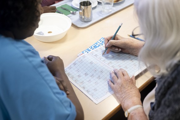 Une refugiee en stage d&#039;auxiliaire de sante regarde une residente faire des mots croises, lors d&#039;une visite sur le lieu de stage de refugies formes aux metiers du domaine de la sante du cent ...