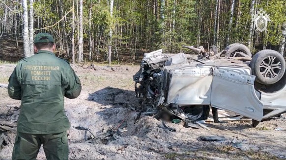 This image taken from video released by the Russian Investigative Committee on Saturday, May 6, 2023, shows a Russian Investigative Committee employee working at the site of the exploded car of Russia ...