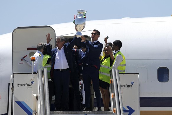 Portugal's Cristiano Ronaldo and coach Fernando Santos, left, lift the Euro 2016 trophy after defeating France in the final, as they arrive at the Humberto Delgado Airport in Lisbon, Portugal, Mo ...