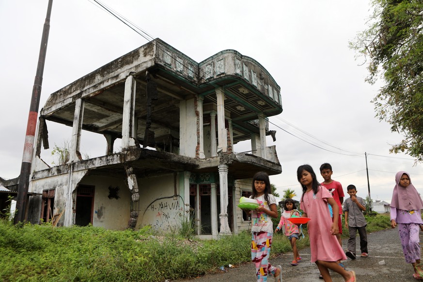 epa10374470 Local people walk in front of the remains of a house that was damaged by the 2004 Indian Ocean earthquake and tsunami, in Banda Aceh, Indonesia, 20 December 2022. On 26 December 2022 Indon ...