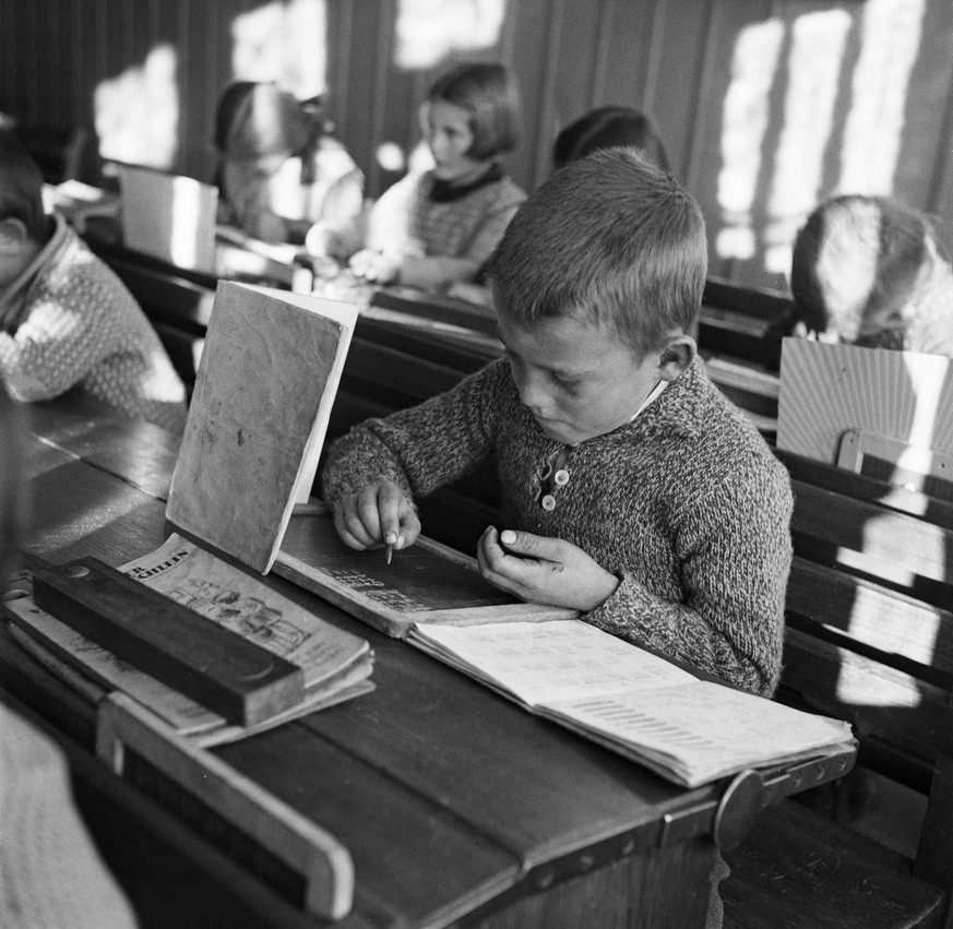 Kinder in der Schule in einem Bergdorf in der Schweiz schreiben einen Rechnungstest, aufgenommen um 1930. Auf den Pulten sind Hefter aufgestellt, um den Einblick des Banknachbars auf die eigenen Resul ...