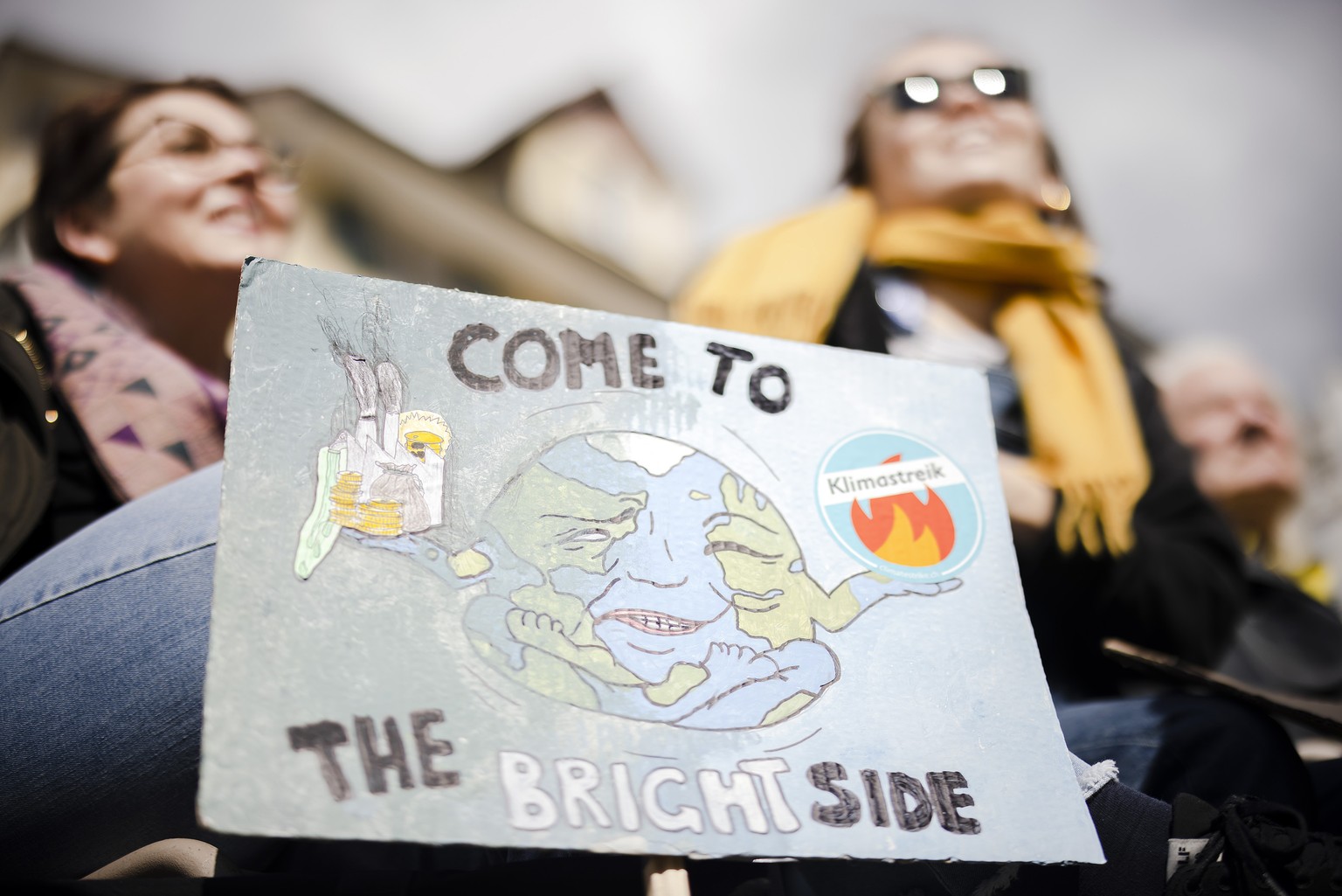 Protesters show a placard reading &quot;come to the bright side&quot; as they take part in a climate strike rally calling for work hours to be reduced, in Zurich, Switzerland, on Saturday, April 9, 20 ...