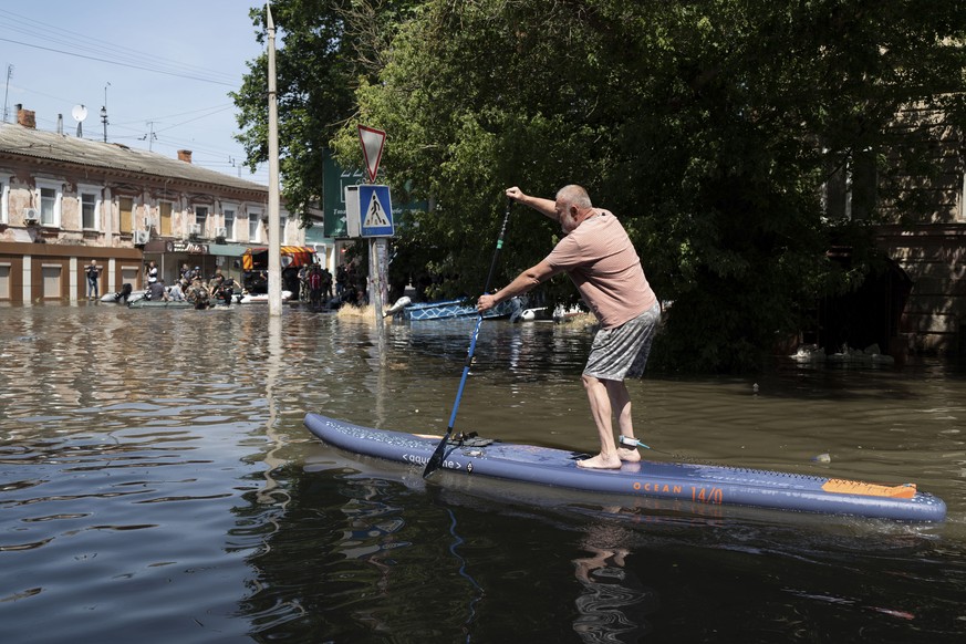 A man uses a stand up paddle board to reach his house in a flooded neighborhood in Kherson, Ukraine, Wednesday, June 7, 2023 after the Kakhovka dam was blown up. Residents of southern Ukraine braced f ...